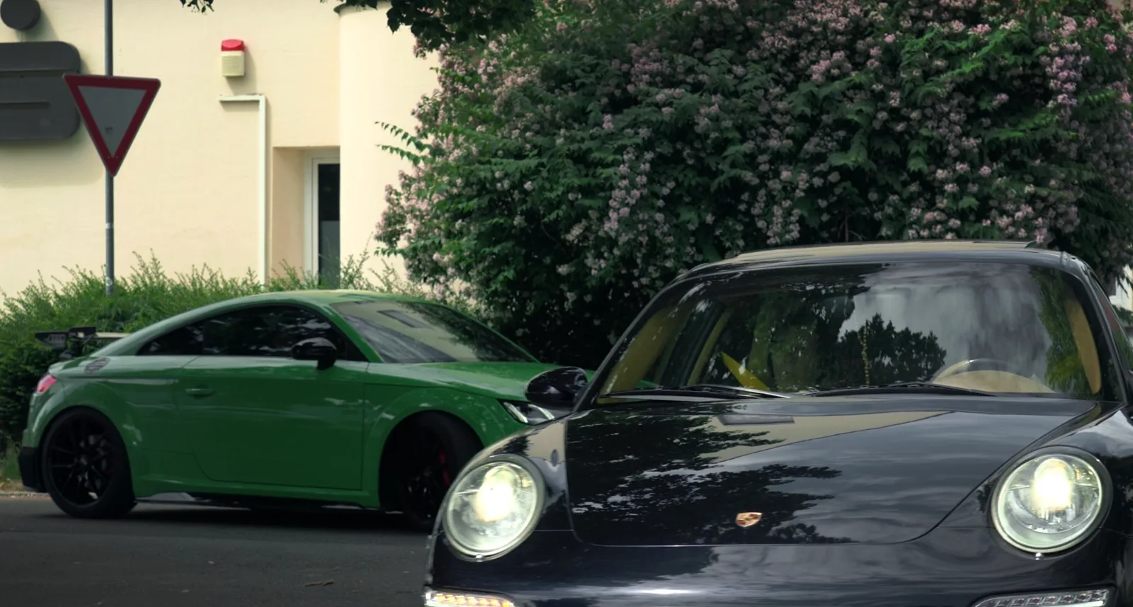 Schwarzer Porsche 911 mit eingeschaltetem Licht, dahinter ein grüner Audi TT
