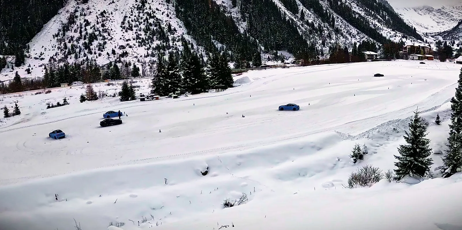 Mehrere Sportwagen auf einer verschneiten Fahrfläche im Tal, von oben gesehen