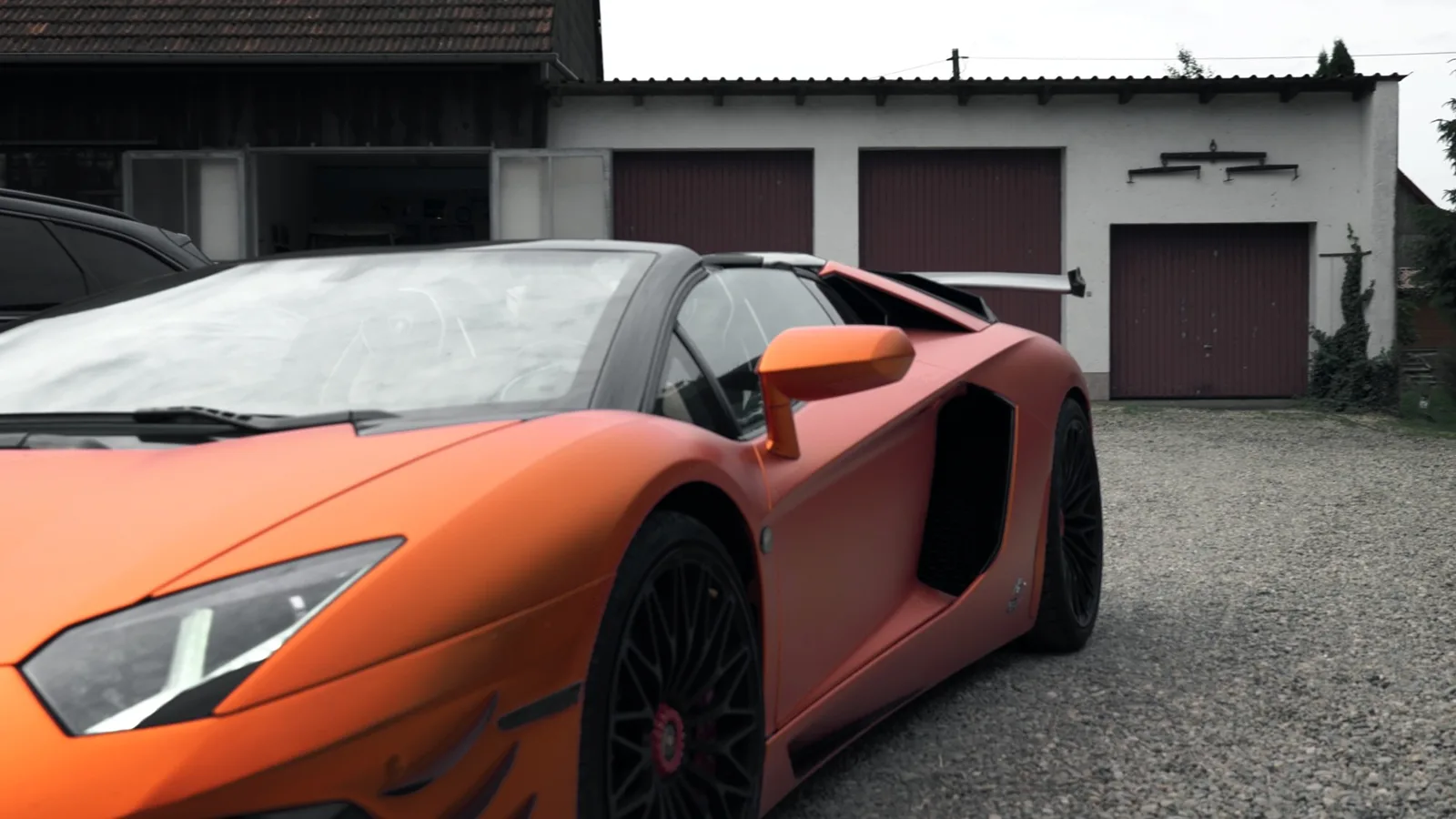 Mattorangefarbener Lamborghini mit offenem Dach vor einer Garagenzeile