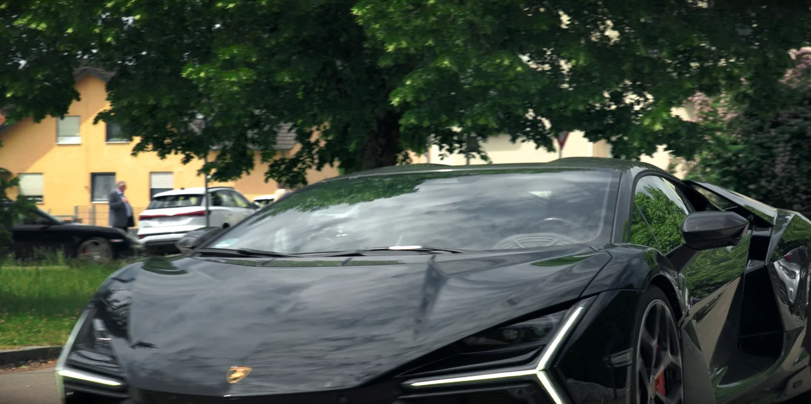 Schwarzer Lamborghini mit leuchtendem Tagfahrlicht unter Bäumen