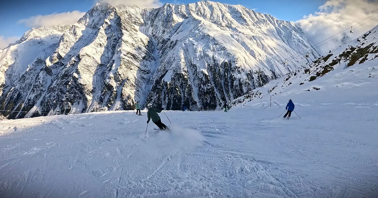 Skifahrer auf einer Piste vor einer steilen, verschneiten Bergflanke