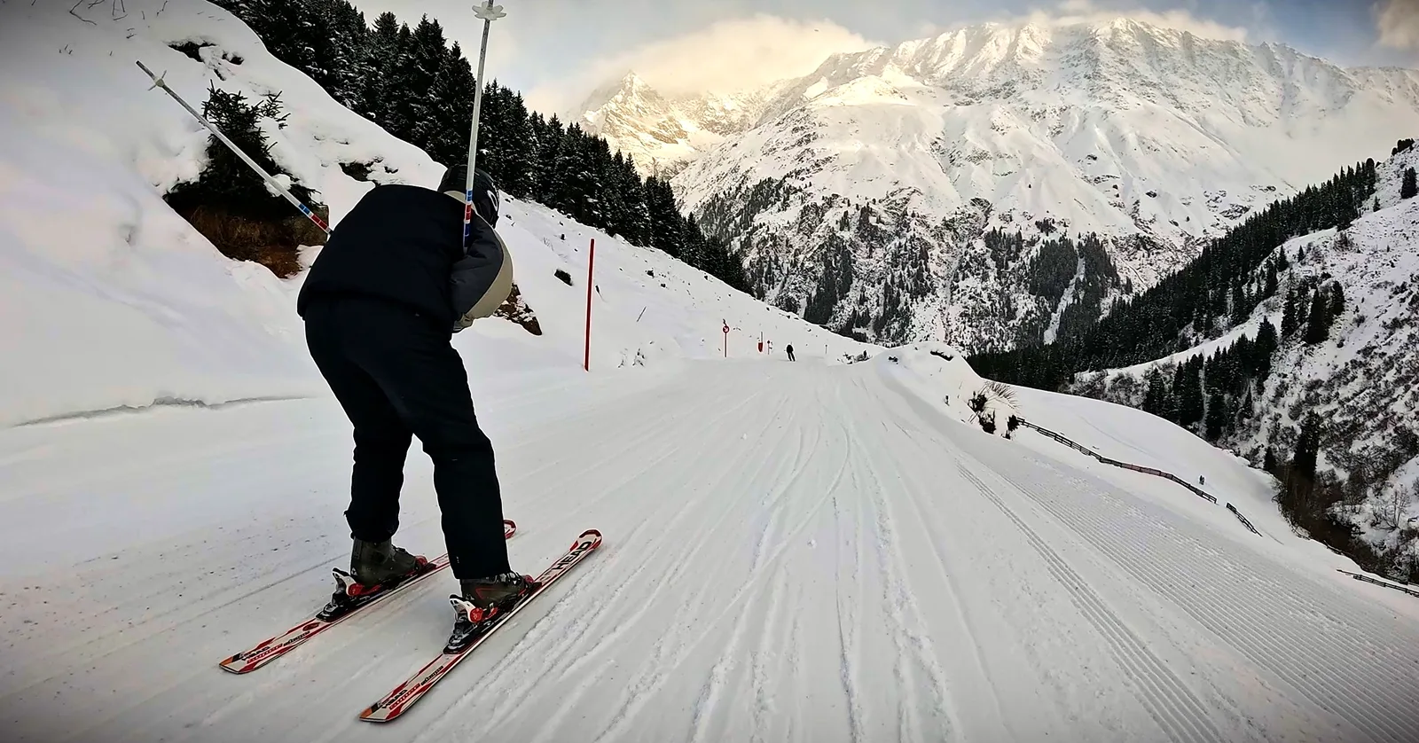 Skifahrer in der Hocke auf einem Ziehweg, vor ihm ein verschneites Bergmassiv