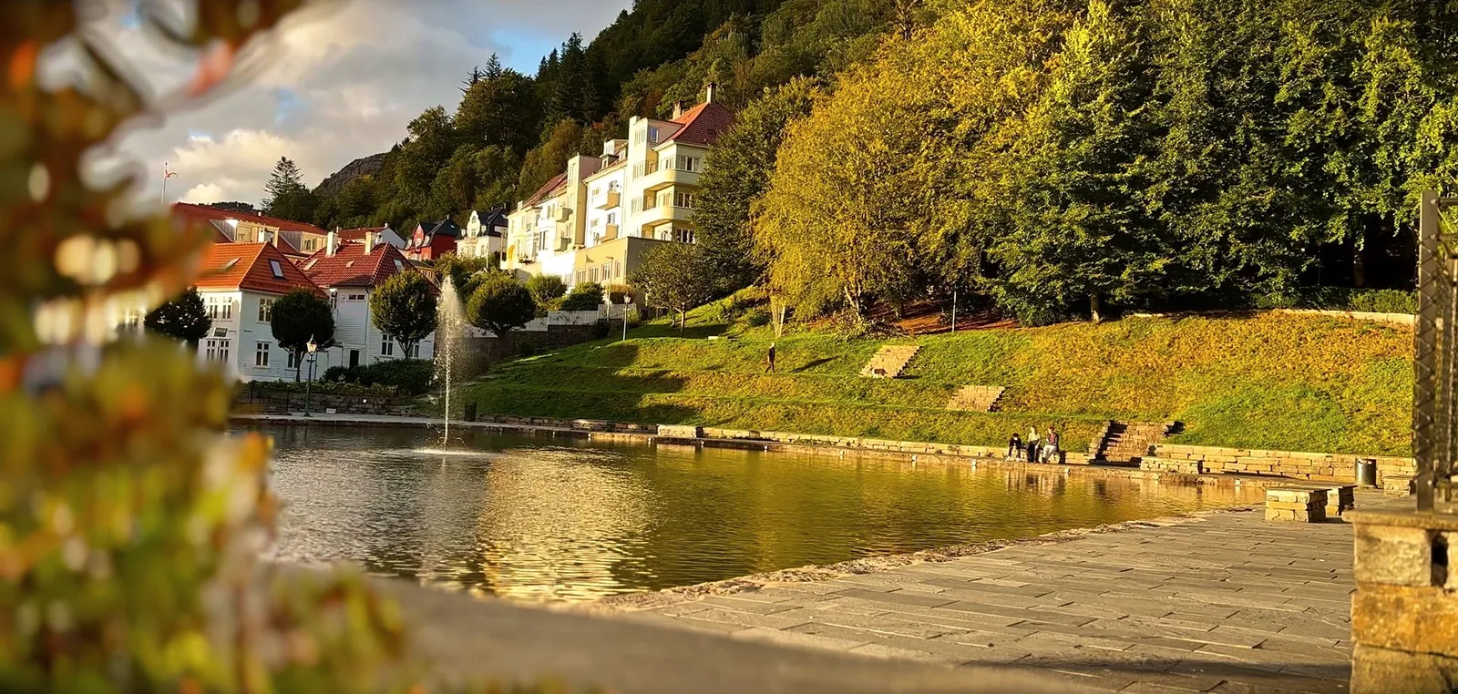 Teich mit Fontäne vor weißen Villen und herbstlich gefärbten Bäumen