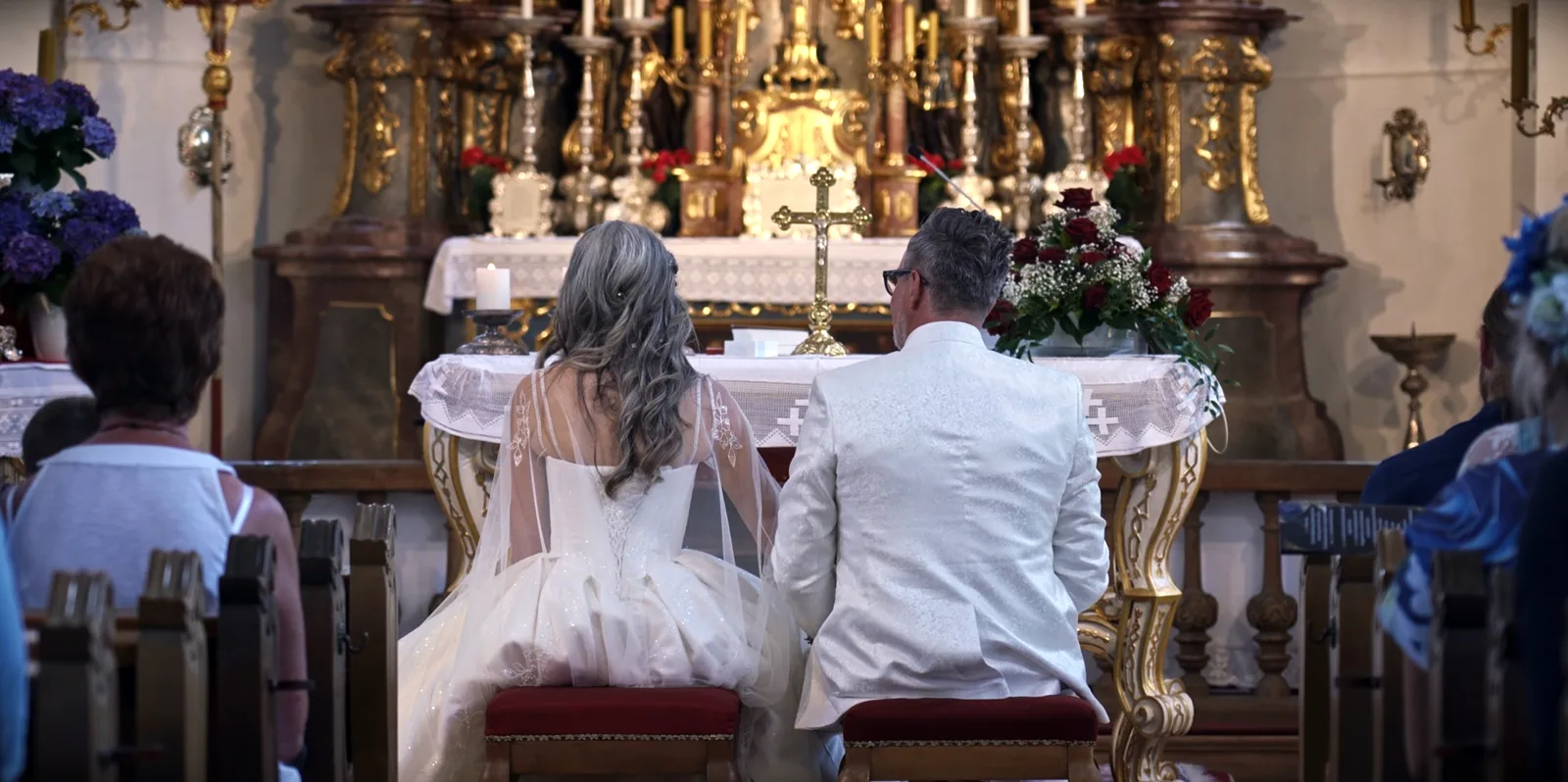 Brautpaar von hinten vor einem goldenen Barockaltar, links und rechts Gäste in den Bänken