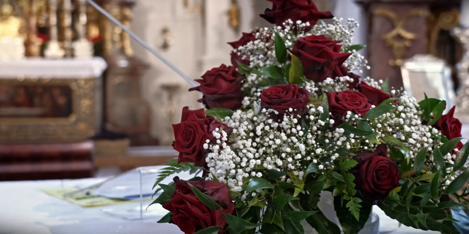 Gesteck aus roten Rosen und Schleierkraut, dahinter unscharf der Kirchenraum