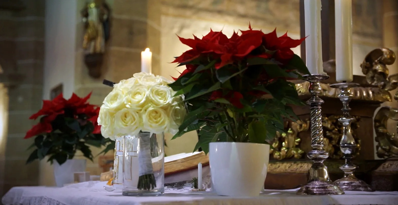 Strauß weißer Rosen neben Weihnachtssternen und einer brennenden Kerze