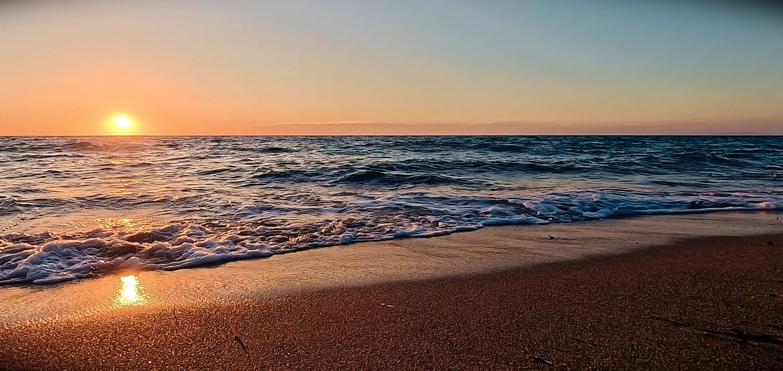 Brandung an einem Sandstrand bei Sonnenuntergang