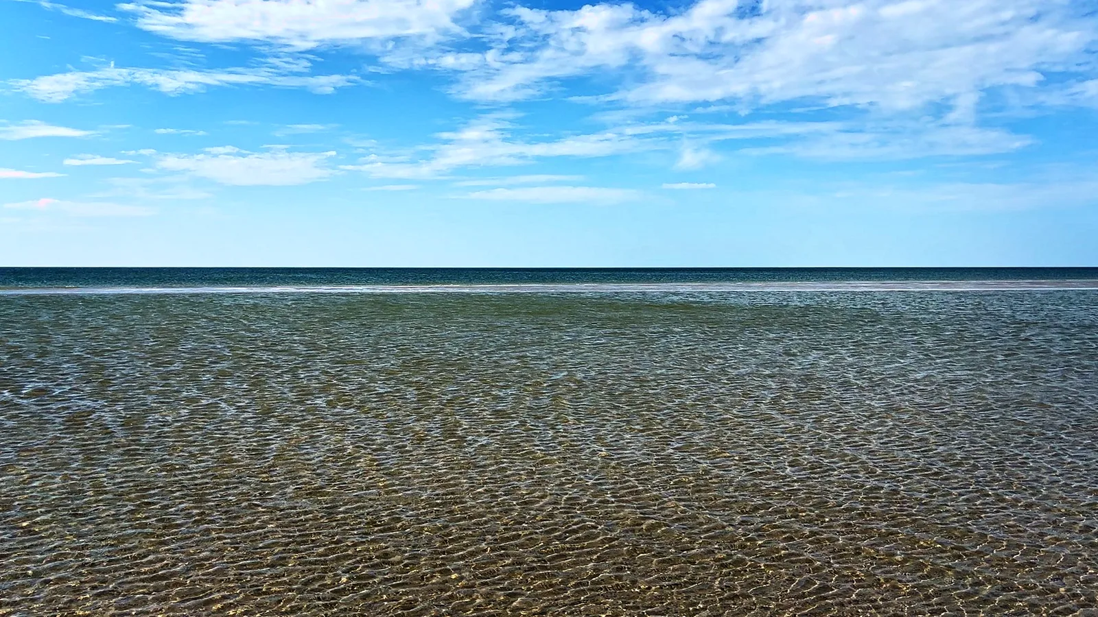 Klares, flaches Meer bis zum Horizont unter einem Himmel mit Schleierwolken