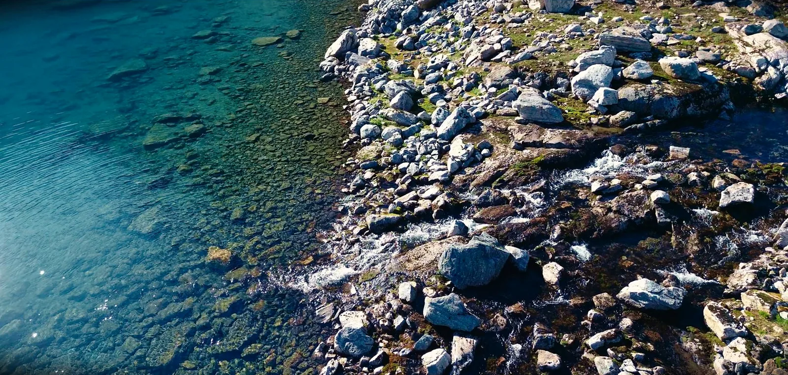 Klares türkisfarbenes Wasser an einem Ufer aus hellen Felsblöcken, von oben gesehen