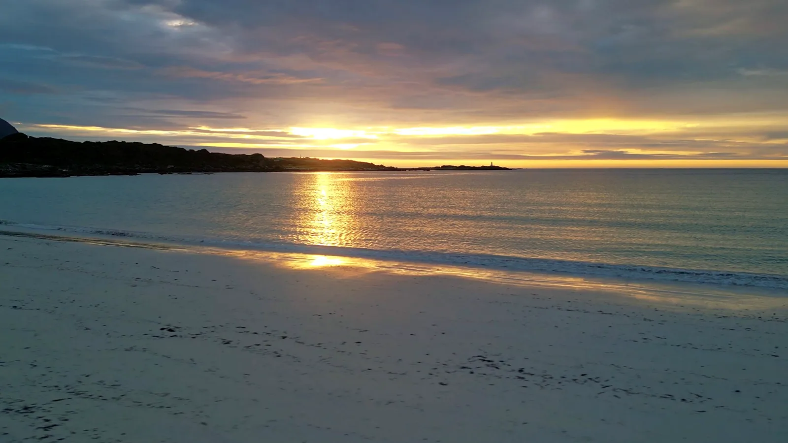 Sandstrand bei Sonnenuntergang, die tief stehende Sonne spiegelt sich im flachen Wasser