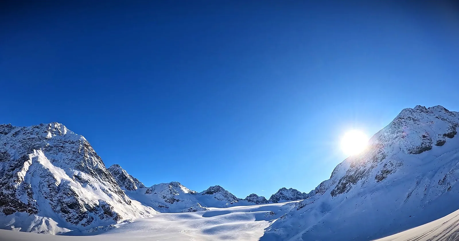 Tief stehende Sonne über einem verschneiten Hochtal unter klarem Himmel