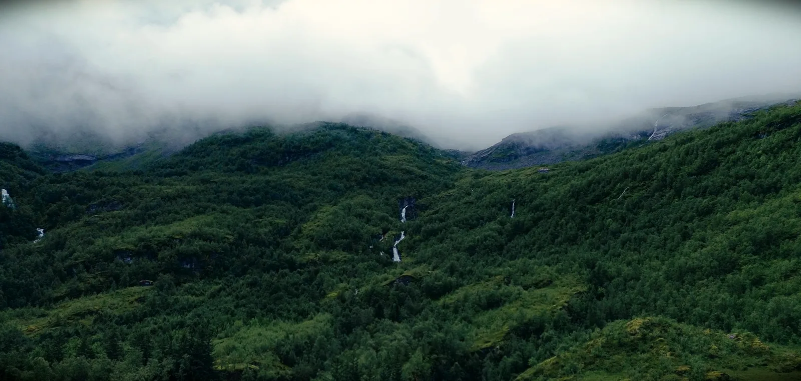Tief hängende Wolken über grünen Berghängen mit schmalen Wasserfällen
